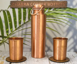 Handcrafted 100% pure copper water bottle with seven colorful chakra symbols engraved vertically. Features a polished metallic finish and a secure screw-top lid on a minimalist white background.